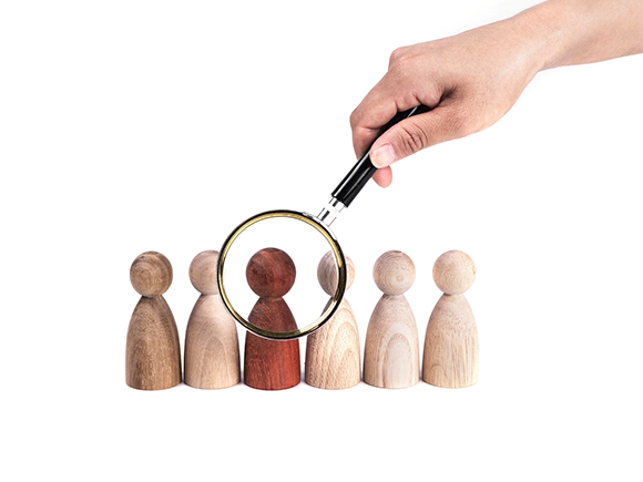 Hand holding a magnifying glass over a red figurine in a row