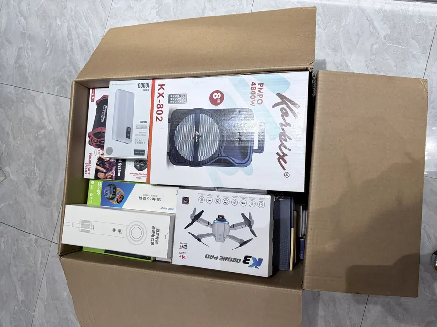 Mixed wholesale carton viewed from above showing the electronics layer and the packed items underneath